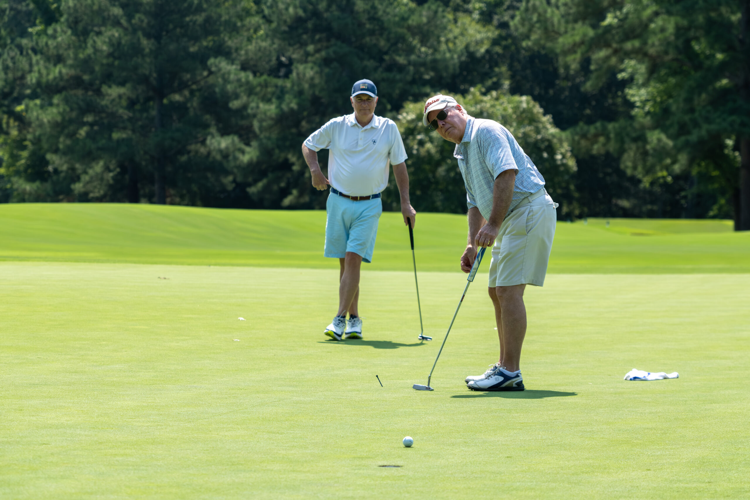 Two men on a golf course, one putting for a ball near a hole.