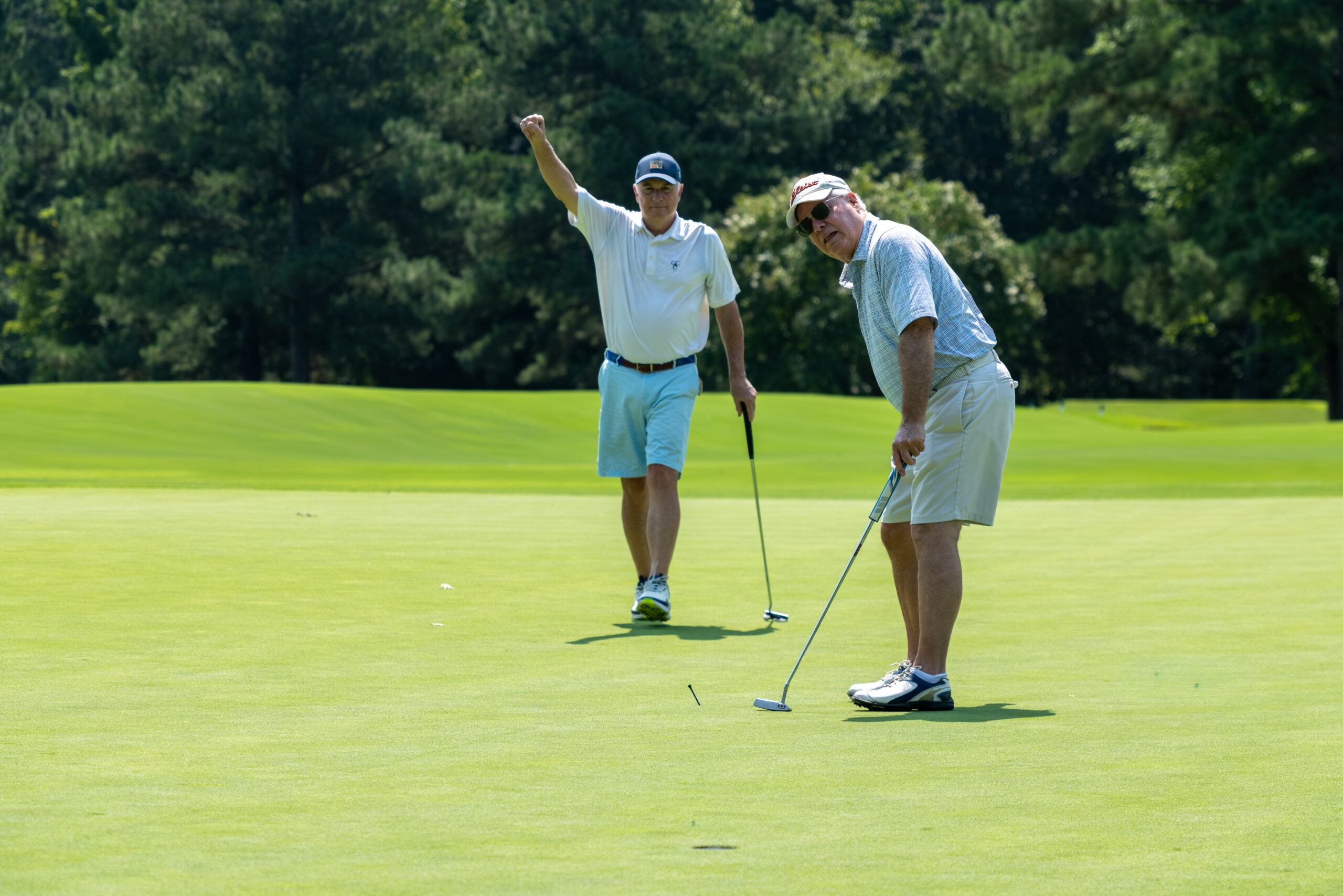 Two men on a green golf course, one cheering and the other putting.