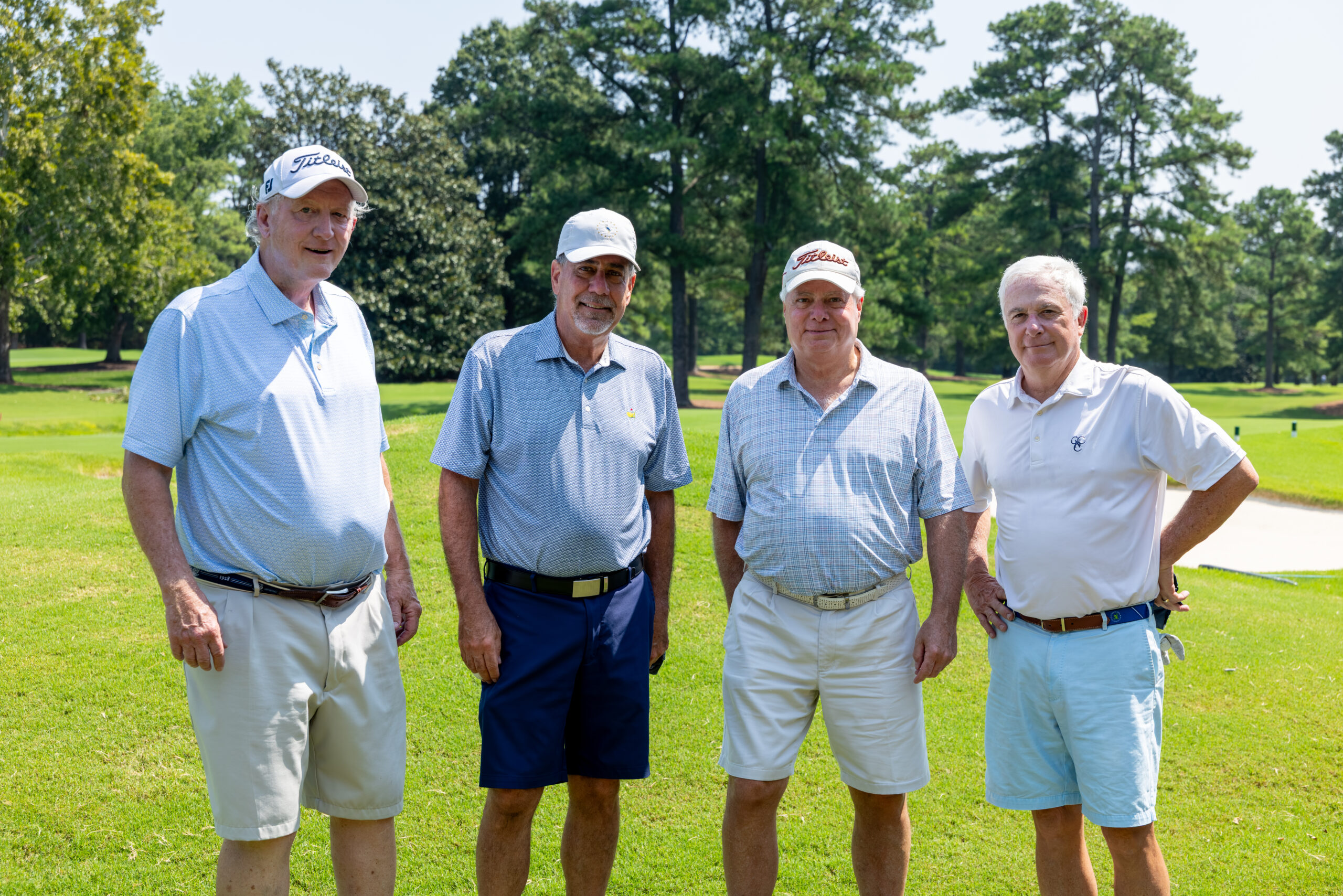 Four men in golf attire standing together on a golf course under a clear sky.