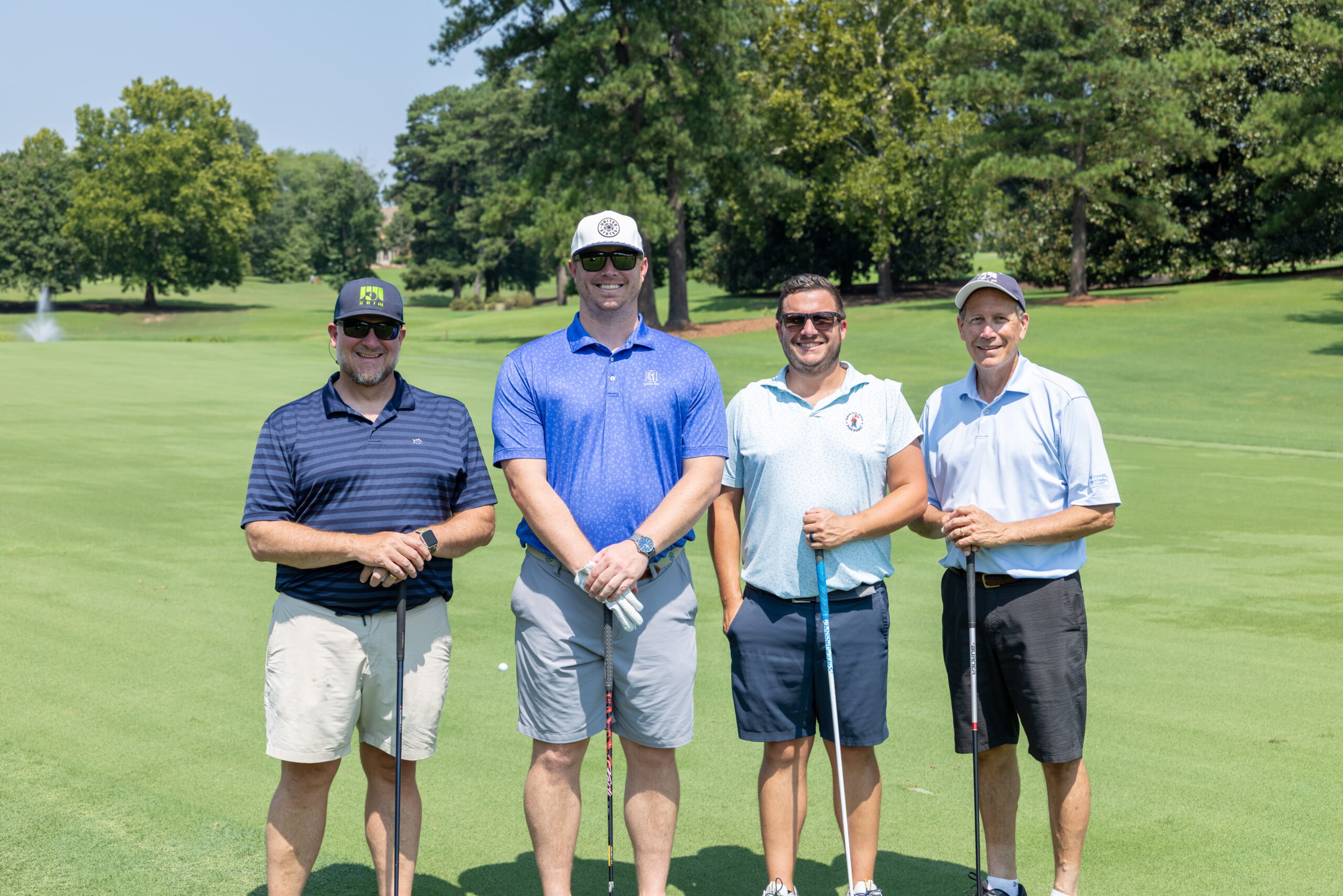 Four men in golf attire standing together on a green, holding clubs.