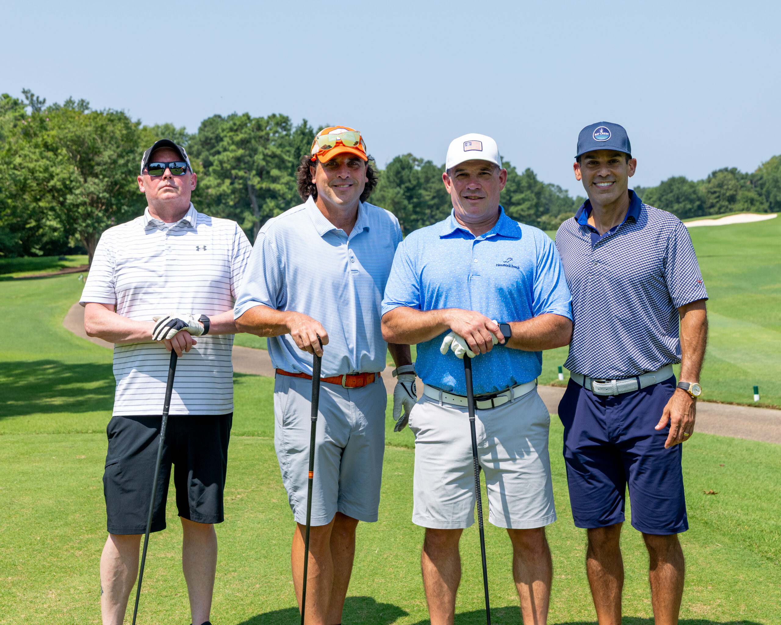 Four men in golf attire standing together on a green, holding clubs.