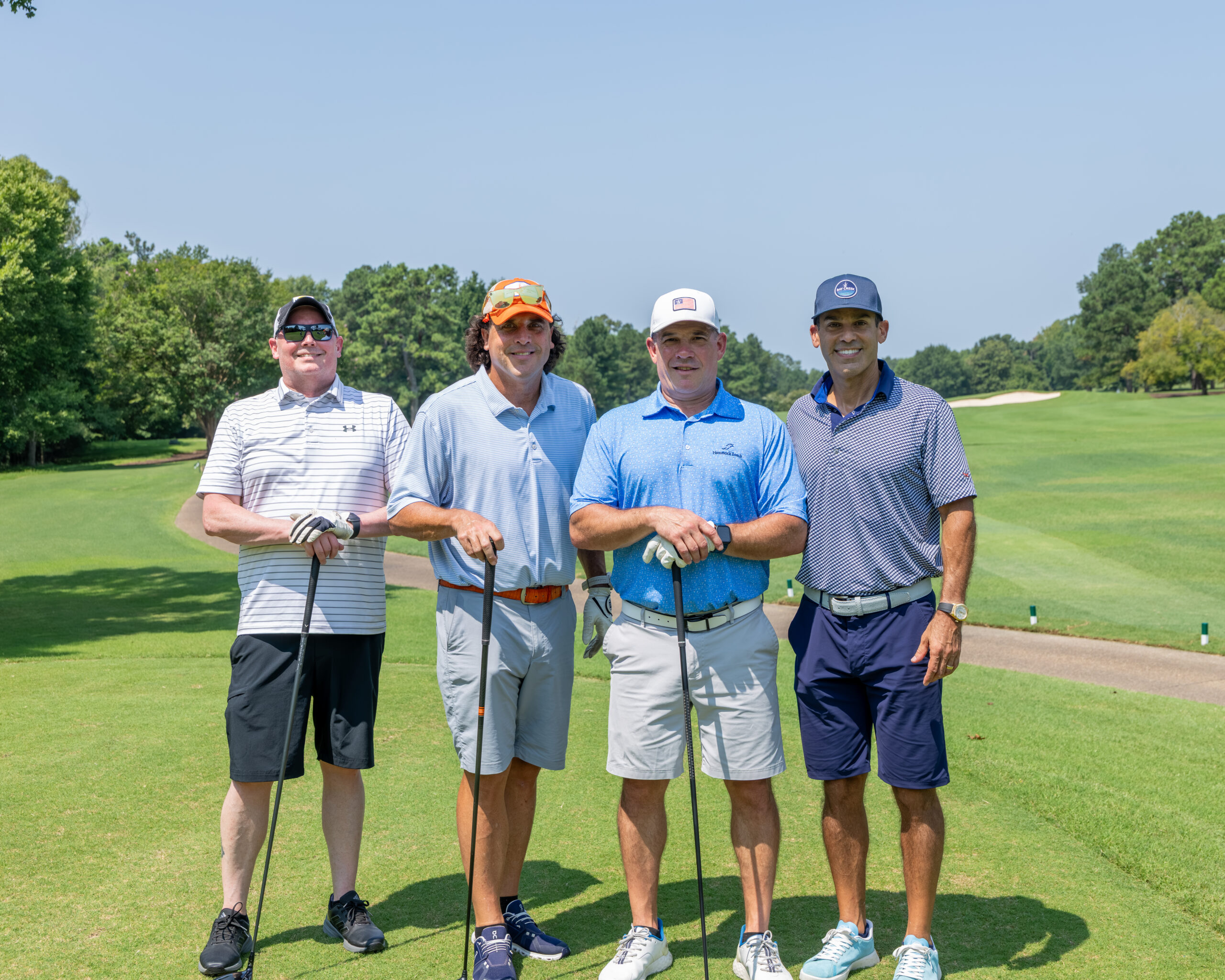 Four men on a golf course standing together and smiling at the camera.